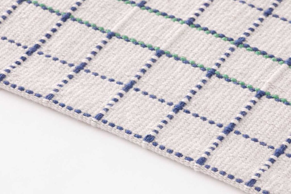 Dettaglio tappeto RETI GAN di Studio Terhedebrügge con motivo a griglia blu-verde su fondo chiaro in PET riciclato