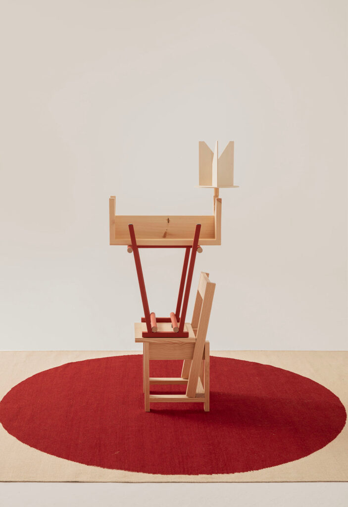 Tappeto rosso Topo di Nanimarquina con sedia in legno, banco rovesciato con gambe rosse e libreria minimale.