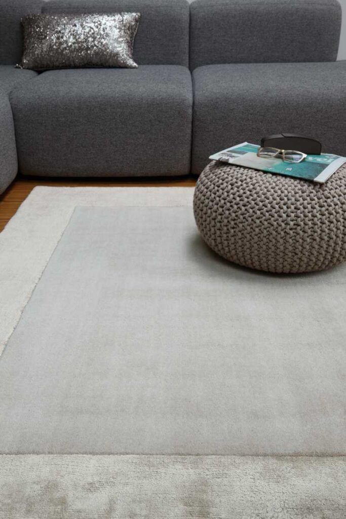 Tappeto Ascot Silver di Asiatic Carpets in lana e viscosa in un soggiorno moderno con divano grigio e pouf beige