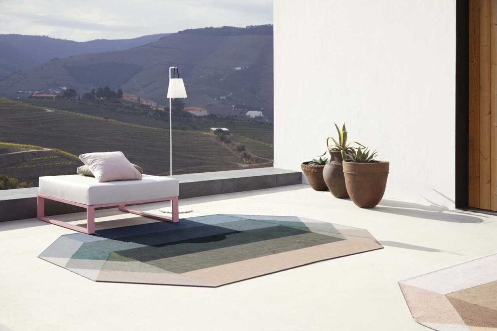 Tappeto GAN Diamond Nude-Petrol su terrazza con vista collinare, design geometrico in PET riciclato